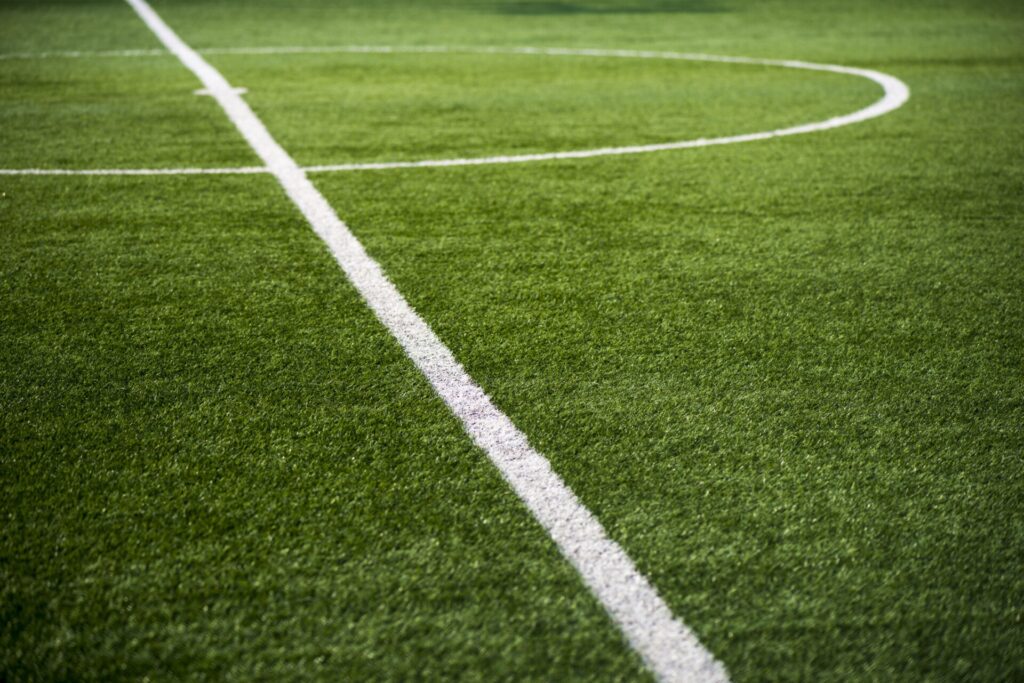 A close-up view of the center circle and lines on a green, well-maintained football field with no people present.